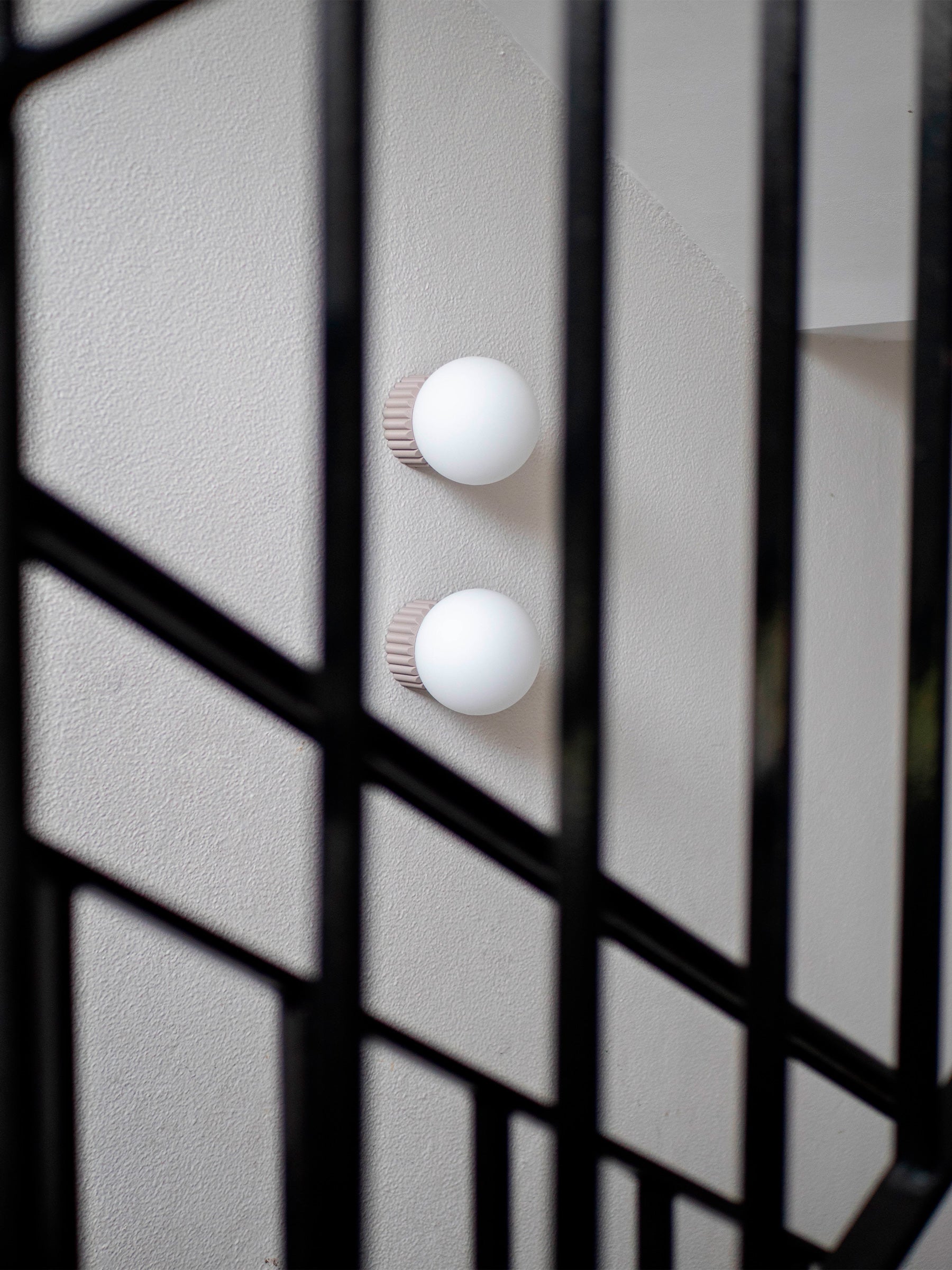 La Quincaillerie moderne - Appliques "Colonnade", globe en opaline mate ø 15 cm, socle taupe à larges cannelures. À Paris, dans les escaliers d'une copropriété. 